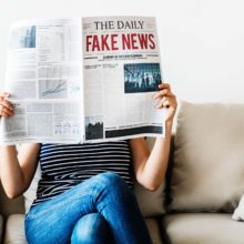 Woman reading newspaper with headline: fake news