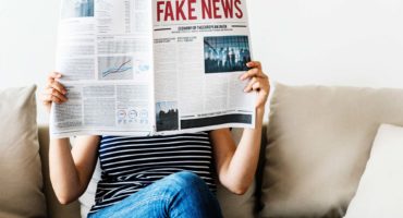 Woman reading newspaper with headline: fake news
