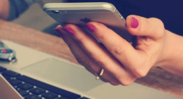 lady's hand hold phone whilst sitting at laptop