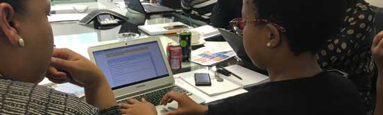 one woman looks on as another types into a laptop