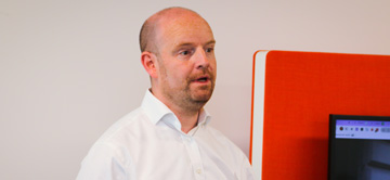 man speaking infront of large monitor