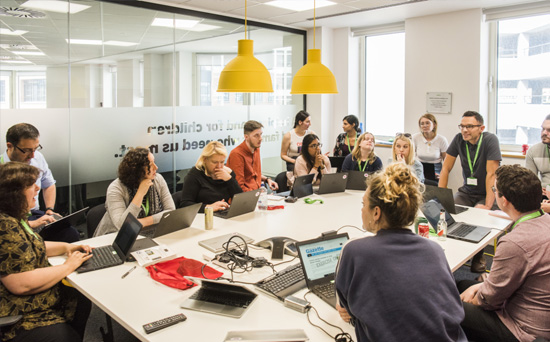 people sitting around a desk at laptops speaking and looking animated